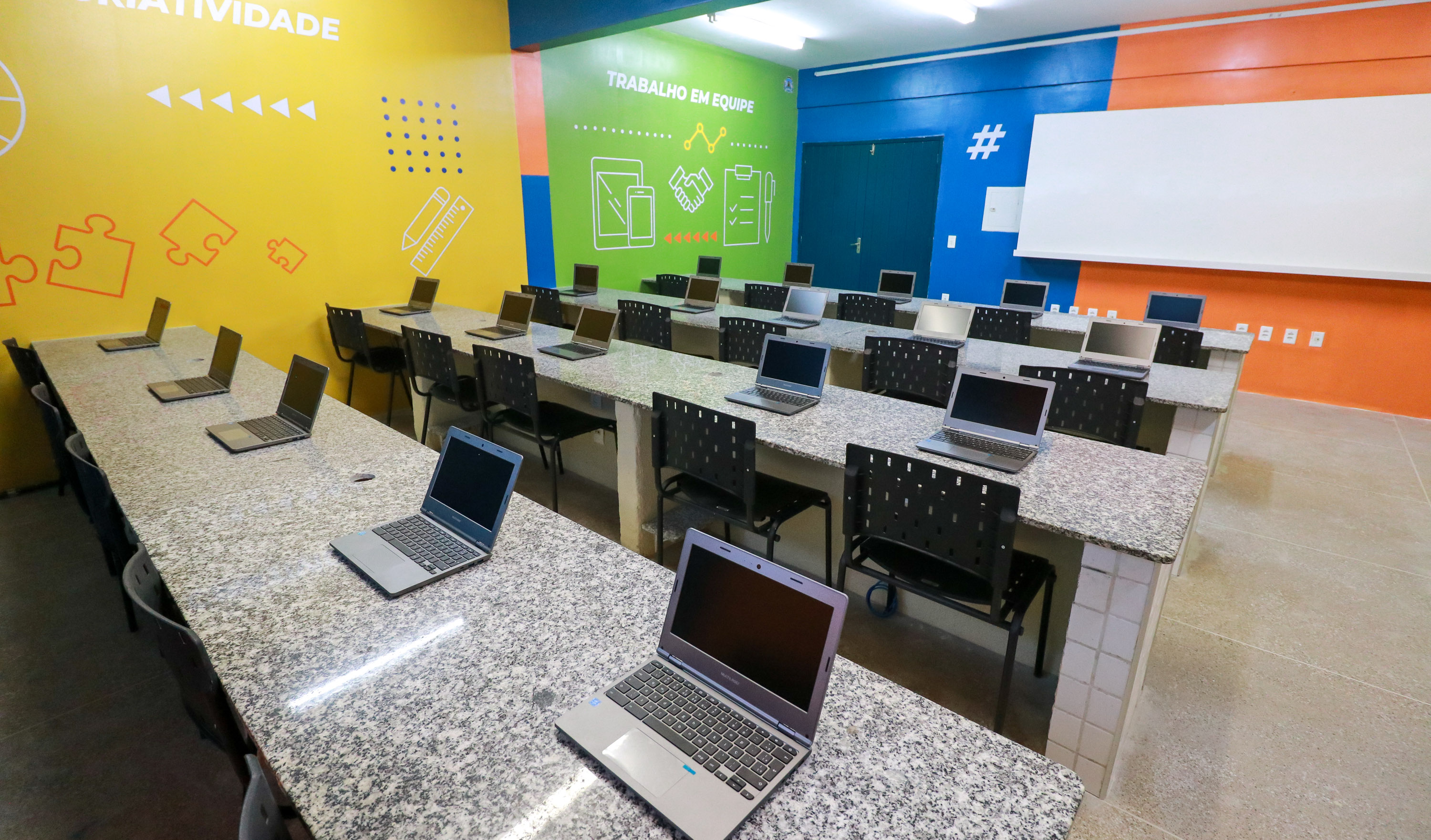 laboratório de informática com bancadas e vários notebookes em cima